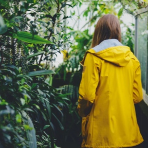 Willow with her back turned to the camera, standing in a green leafy garden wearing a bright yellow raincoat